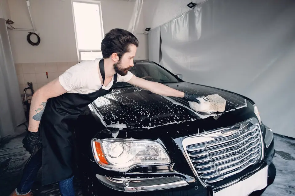 expert hand washing a car after soap cleaning